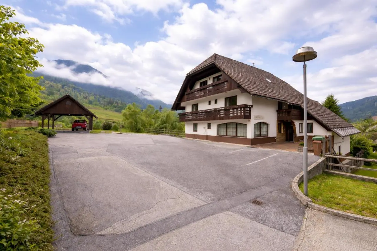Hiša Apartmaji Bor z lesenimi balkoni, parkirišče pred njo in gore v ozadju
